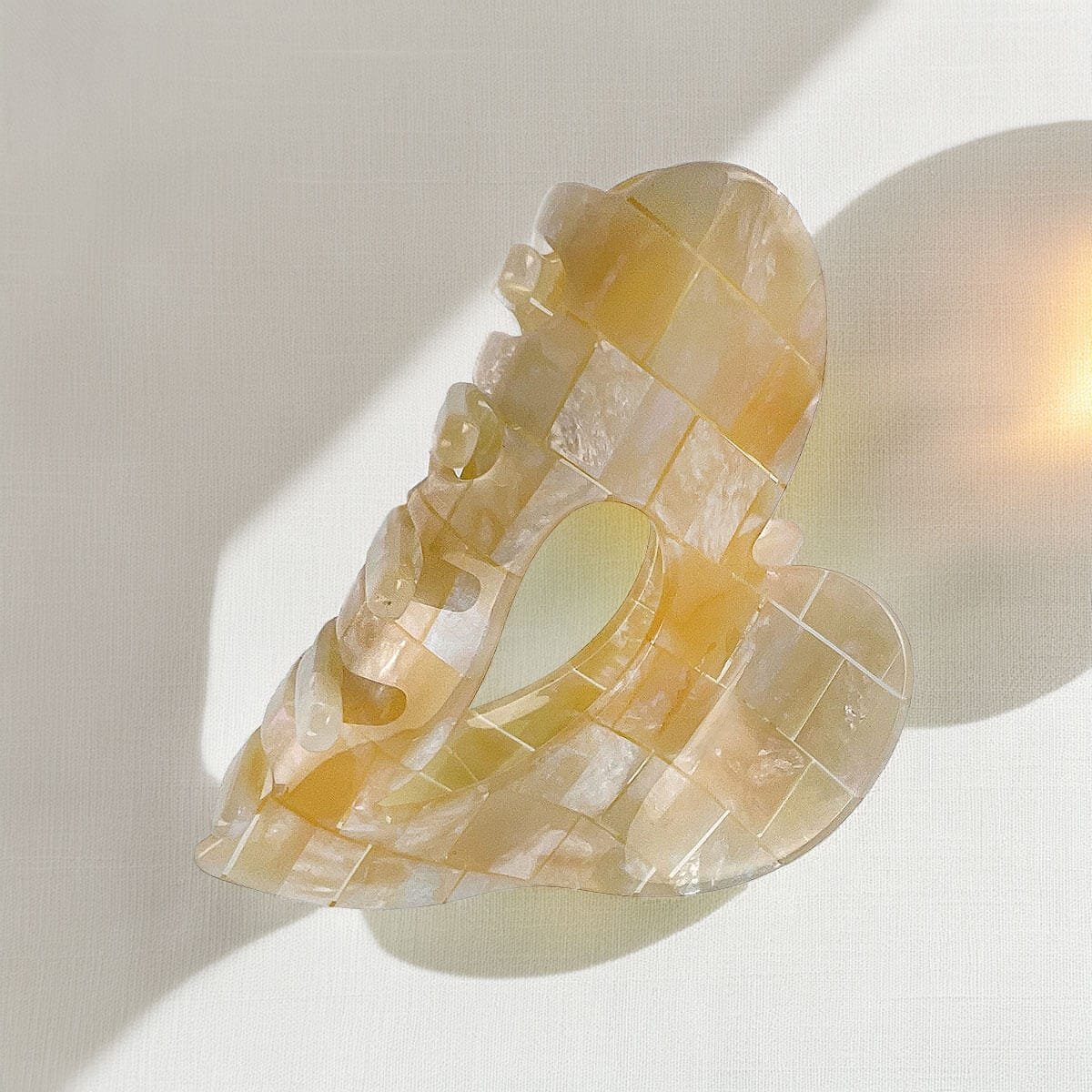 Pince à cheveux en acétate nacré sur fond crème nacré, ombre douce, rendu premium