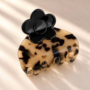 Pince à cheveux fleur noire en acétate coloris écaille miel, posée sur fond crème